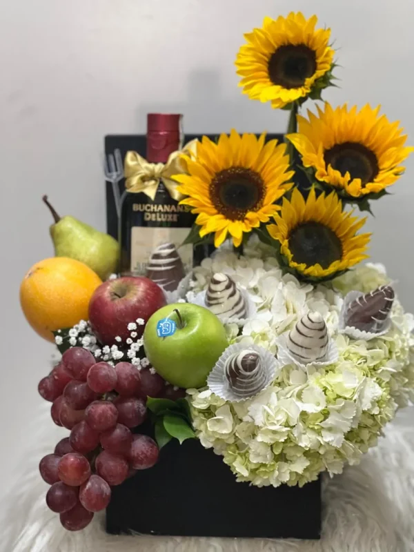 Caja con girasoles, ortensias, fresas con chocolate, frutas y botella de Buchana's