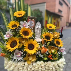 Arreglo floral en rosas blancas, con girasoles, lirios, orquideas, chocolates Ferrero Rocher y virgen de marmolina.