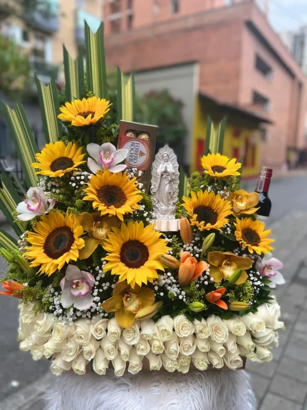 Arreglo floral en rosas blancas, con girasoles, lirios, orquideas, chocolates Ferrero Rocher y virgen de marmolina.